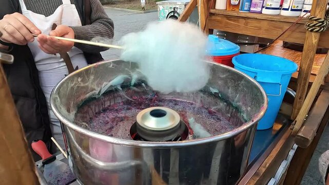 A man is making candyfloss in a silver bowl at a street fair stall.