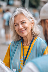 A woman with gray hair smiles while engaging with another volunteer at a bustling community event in daylight