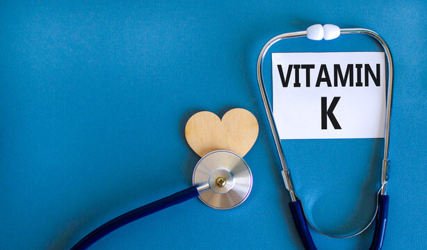 Vitamin K phylloquinone symbol. Concept words Vitamin K on beautiful white card. Wooden heart and stethoscope. Beautiful blue background. Medical healthy lifestyle Vitamin K phylloquinone concept.