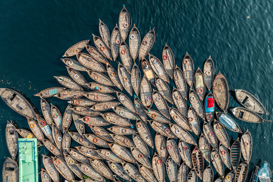 Aerial view of traditional boats clustered together on the shimmering, dark waters, creating a mosaic of textures and tones, Dhaka, Dhaka District, Bangladesh.