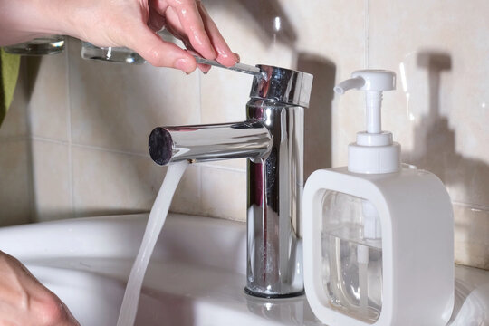 Close-up of a hand shutting off running water in bathroom sink to reduce utility bills and save water resources