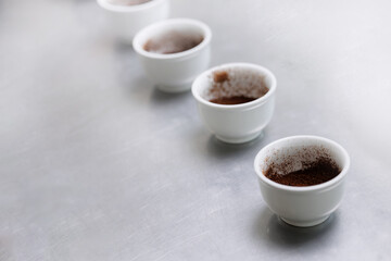 Coffee factory tasting, white cups with ground coffee on stainless steel surface, top view