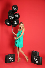 Happy woman with purchases on red background. Shopping bags and balloons with percent signs....