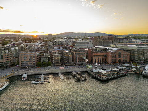 Aerial view of the Aker Brygge waterfront district basking in the golden light of dusk, casting long shadows across the water, Oslo, Norway.