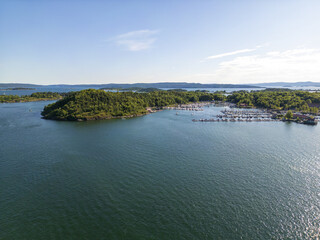Aerial view of islands cloaked in verdant forests meet the tranquil, sun-kissed waters surrounding a bustling marina, Oslo, Norway.