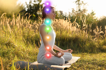 Woman meditating in Lotus pose in nature. Seven chakras glowing