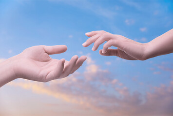 Man and woman reaching to each other against sky at sunset, closeup of hands