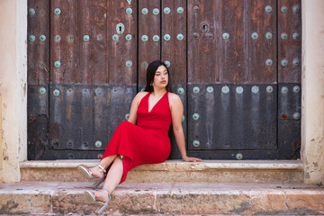 Young, pretty, brunette woman in a nice red party dress and heels, relaxed and calm, sitting on...