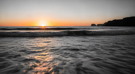 Monochrome beach sunset with soft waves, glowing water reflections and distant cliffs