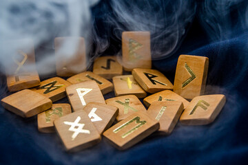 Wooden runes lie on a black background with smoke from above	
