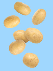 Raw potatoes in air against light blue background