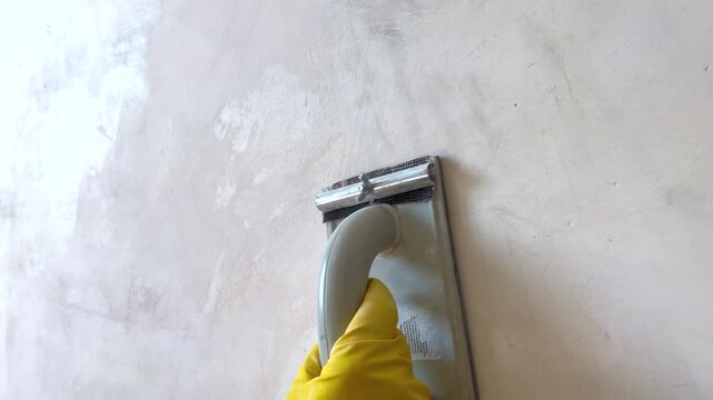 Construction worker sanding wall with hand sander