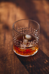 Glass of whiskey with ice and lemon slices on wooden table in rays of light