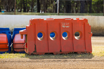Photograph of an old and weathered industrial plastic safety protection barrier located on the infield of a dirt speedway race track on a sunny day. 