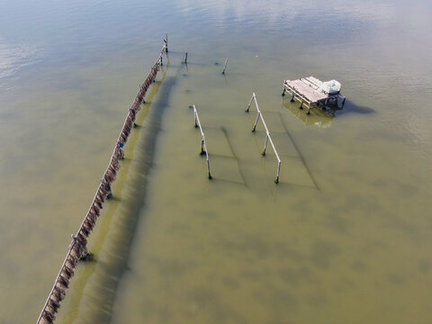 Aerial view of weathered wooden remnants stand starkly against the murky water, contrasting textures creating a somber tableau of decay and stillness, Kalochori, Greece.