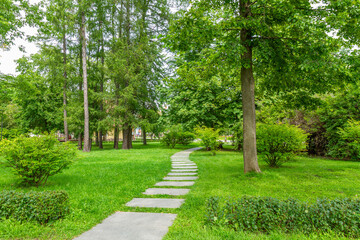 A green park with a winding stone path among trees and bushes.