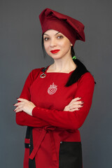 Portrait of a pastry chef in a red apron and a red hat on a gray studio background. Cooking