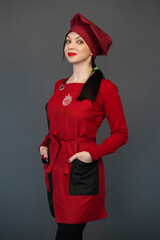 Portrait of a pastry chef in a red apron and a red hat on a gray studio background. Cooking