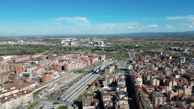 Aerial view of the cityscape with the train station bisecting the residential area under a bright blue sky, Lleida, Spain.