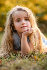 Fototapeta premium portrait of a little girl with long blond hair in a park. girl lying on the grass