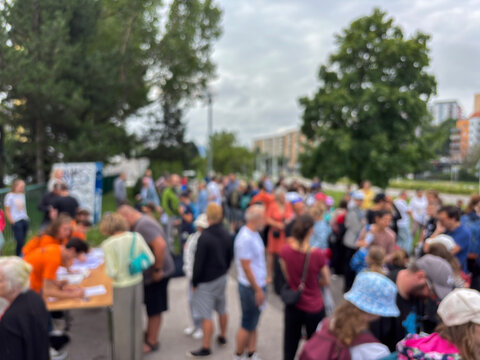 Out-of-focus photo showing a large, blurred crowd gathered at an outdoor event near a registration table in an urban setting.