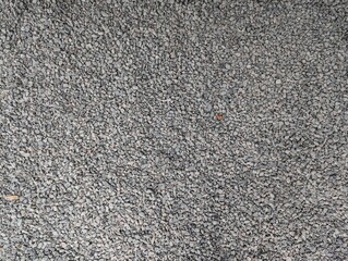Textured gravel ground covered in small gray stones showing intricate patterns and depth during a sunny afternoon