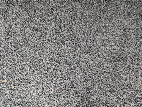 Textured gravel ground covered in small gray stones showing intricate patterns and depth during a sunny afternoon