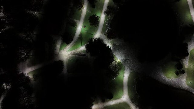 Bursa's Nocturnal Park Illumination: A Drone's Aerial Perspective Over Winding Luminous Paths and Verdant Lawns Amidst Somber Tree Silhouettes Evoking Urban Serenity.