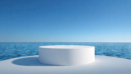 White cylinder pedestal on a light gray surface overlooking a calm ocean.