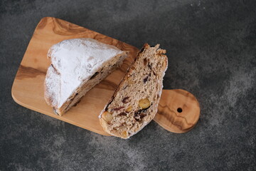 A slice of stollen bread sits on a wooden board, showcasing its texture and ingredients. A festive atmosphere created with decorations nearby, hinting at the holiday season. top view