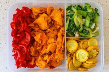 Colorful assortment of sliced red pepper, carrots, bok choy, and yellow zucchini in container