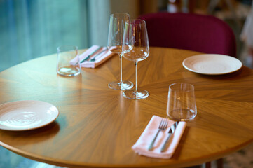 Elegant table setting with empty wine glasses, plates, cutlery, and napkins on a round wooden table...