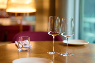 Elegant table setting with empty wine glasses, plates, and napkins on a warm wooden table in a cozy dining space, illuminated by soft ambient lighting and inviting atmosphere