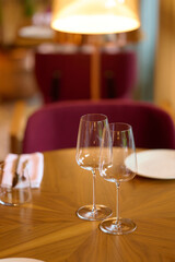 Elegant table setup with two empty wine glasses, plates, and folded napkins on a polished wooden table in a cozy restaurant ambiance, warm lighting creating a romantic atmosphere