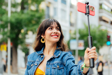 Tourist taking selfie with smartphone and selfie stick in urban environment