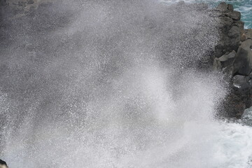 Waves crashing against rocky shore creating a misty spray in coastal landscape during midday
