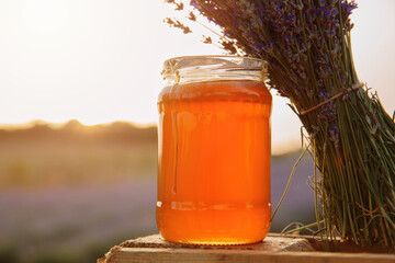 Glass jar filled with golden lavender honey standing next to purple lavender bouquet in warm...