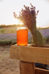Natural lavender honey in a glass jar with lavender bouquet on wooden crate in rural field at sunset