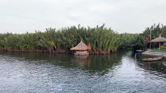 A tranquil river winds through dense mangroves and palm forests beside a remote village in Mataob Maasin, Siargao Islands, Philippines, nestled against green hills under a cloudy sky