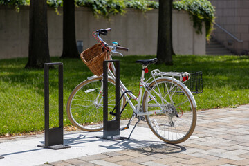 Bike parked at biking rack on the sidewalk. Retro bicycle with wicker basket.