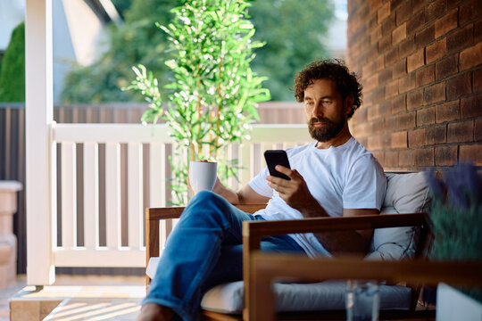 Man using smart phone while having cup of coffee on  porch.