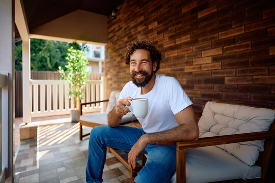 Happy man drinking coffee while relaxing on porch.