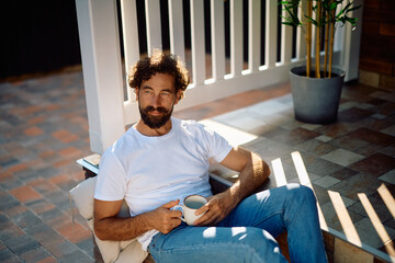 Pensive man with cup of coffee relaxing on porch staircase.