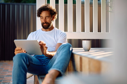 Smiling man using digital tablet while relaxing on porch staircase.