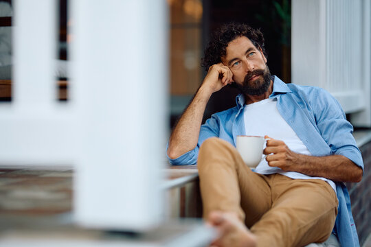 Pensive man having cup of coffee while relaxing on patio at home.