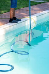 Person cleaning swimming pool with vacuum hose during sunny afternoon at residential backyard