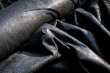 Obraz premium closeup of a thick roll of black landscape fabric partially rolled out for installation. landscaping or construction design element or banner.