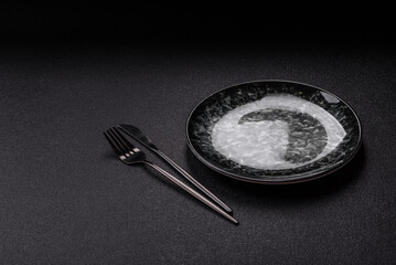 Empty round black plate for food, kitchen utensils on dining table. Empty plate
