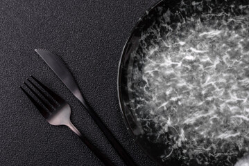 Empty round black plate for food, kitchen utensils on dining table. Empty plate