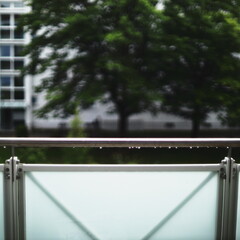 raindrops, balcony railing, blurred background, modern architecture, green trees, glass panel,...